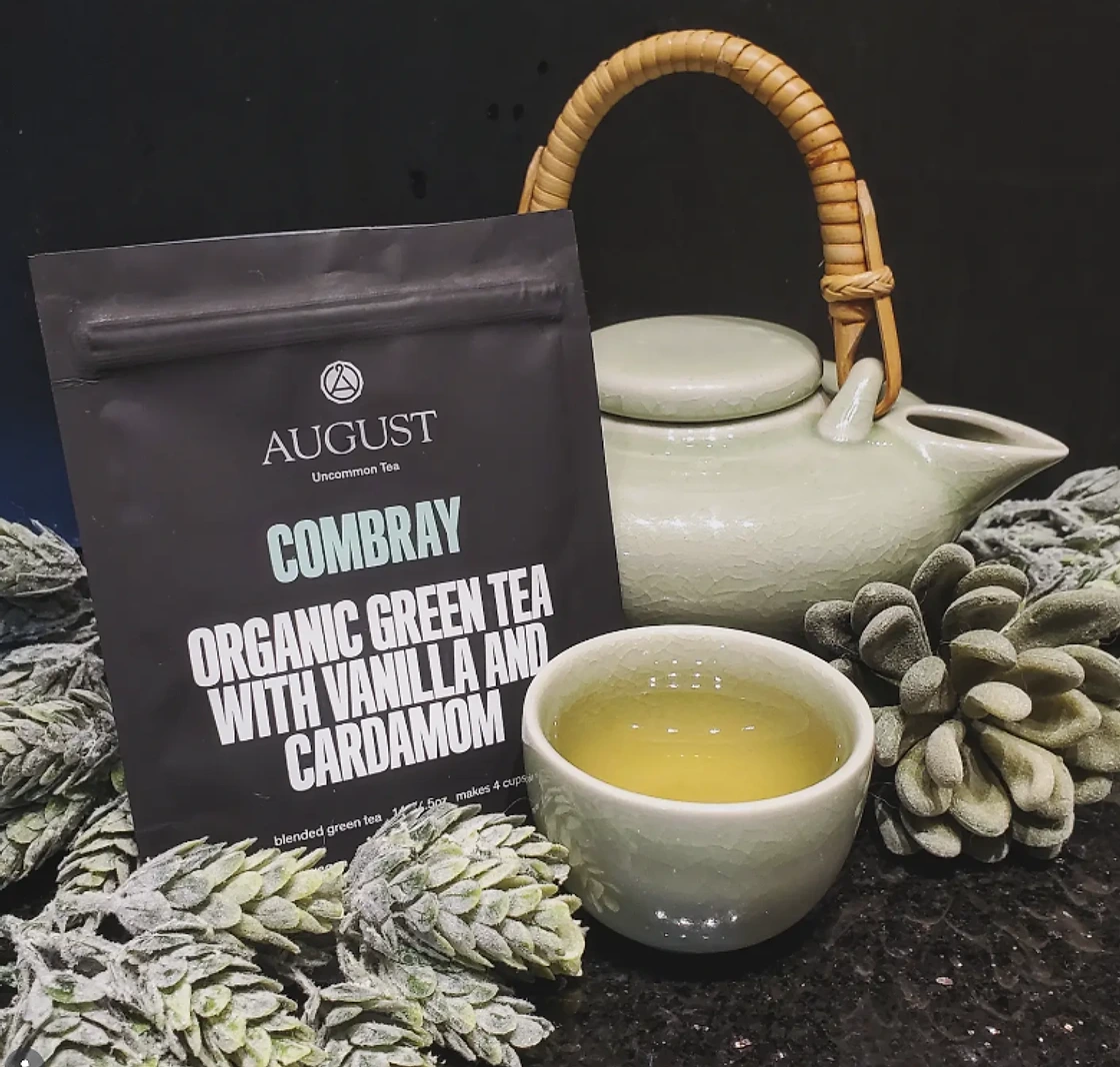 An August Uncommon Combray green tea pouch beside a green teapot and cup of tea