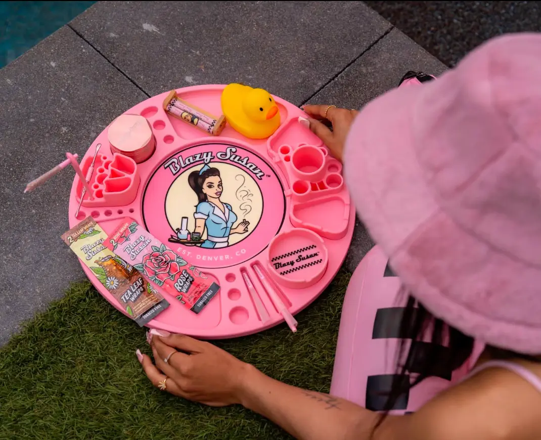 A pink Blazy Susan rolling tray with rose wraps and a rubber duck, beside a person in a pink bucket hat
