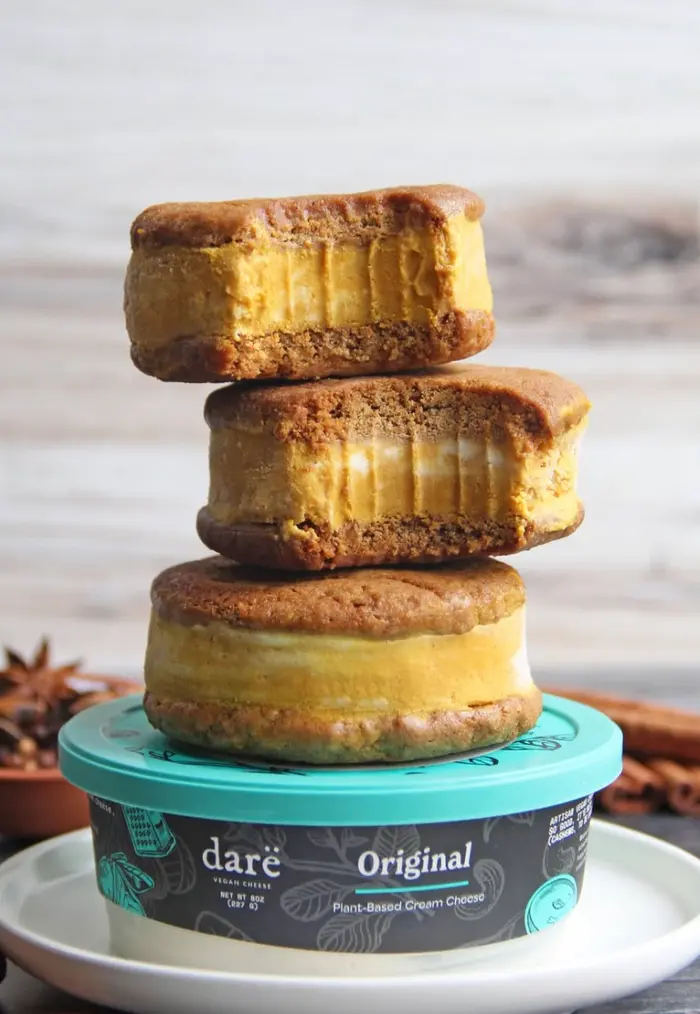 Three pumpkin cookie sandwiches stacked on a teal Darë Original plant-based cream cheese tub