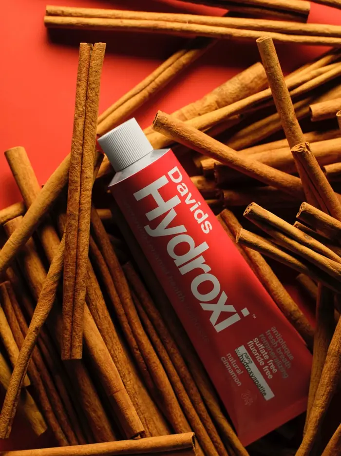 A red Davids Hydroxi cinnamon toothpaste tube lying on a pile of cinnamon sticks