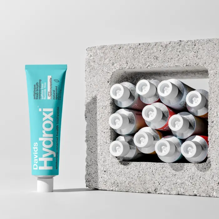 A Davids Hydroxi toothpaste tube standing beside a concrete block filled with toothpaste tubes