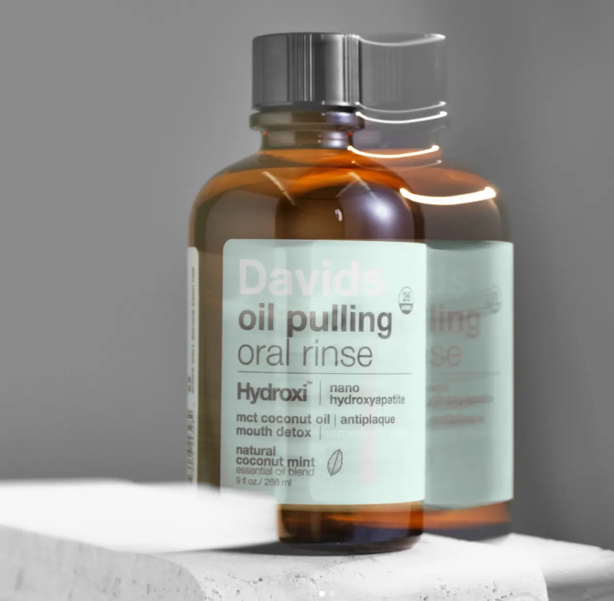 A Davids oil pulling oral rinse in an amber glass bottle on a pale concrete block