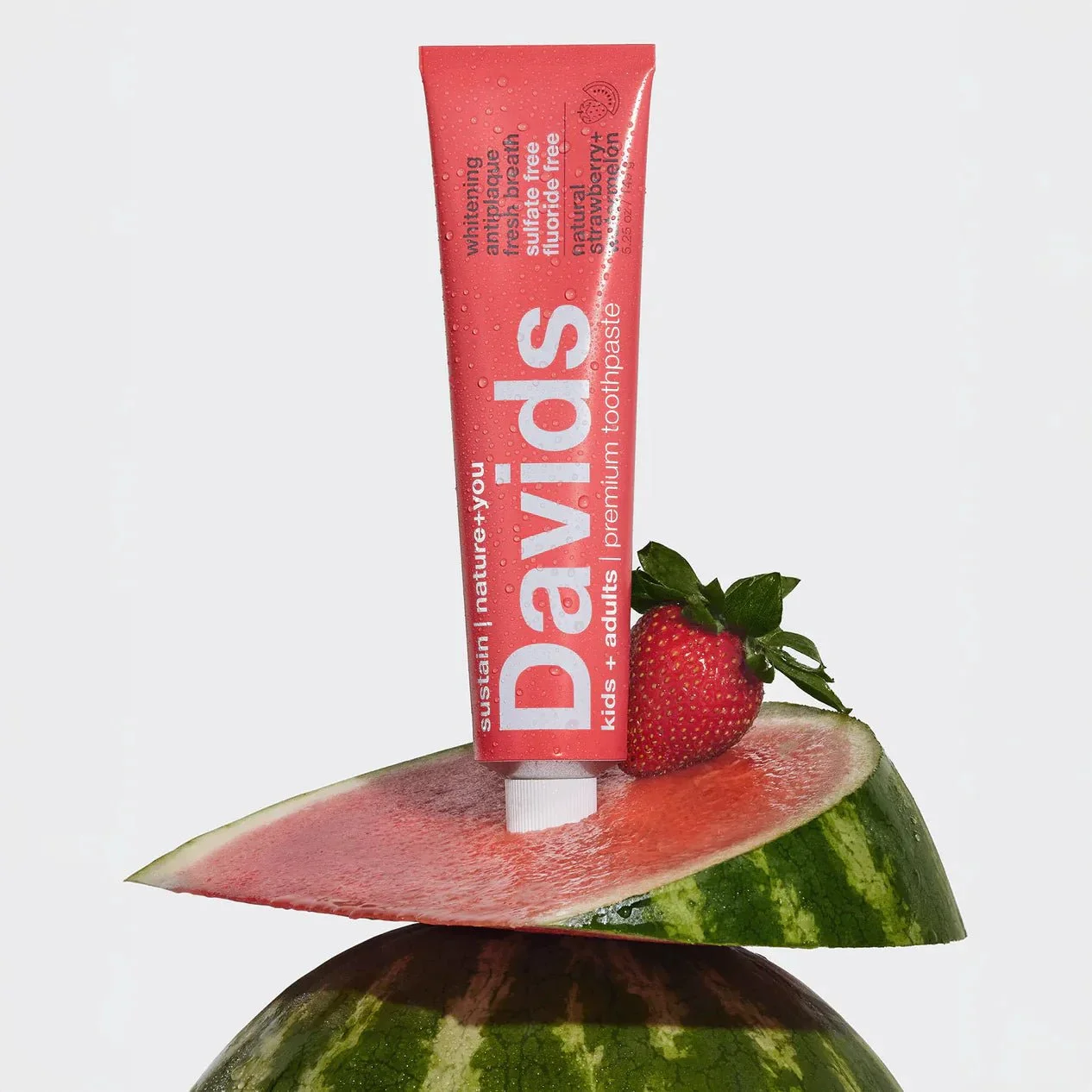 A tube of Davids strawberry and watermelon toothpaste balanced on a slice of watermelon with a strawberry
