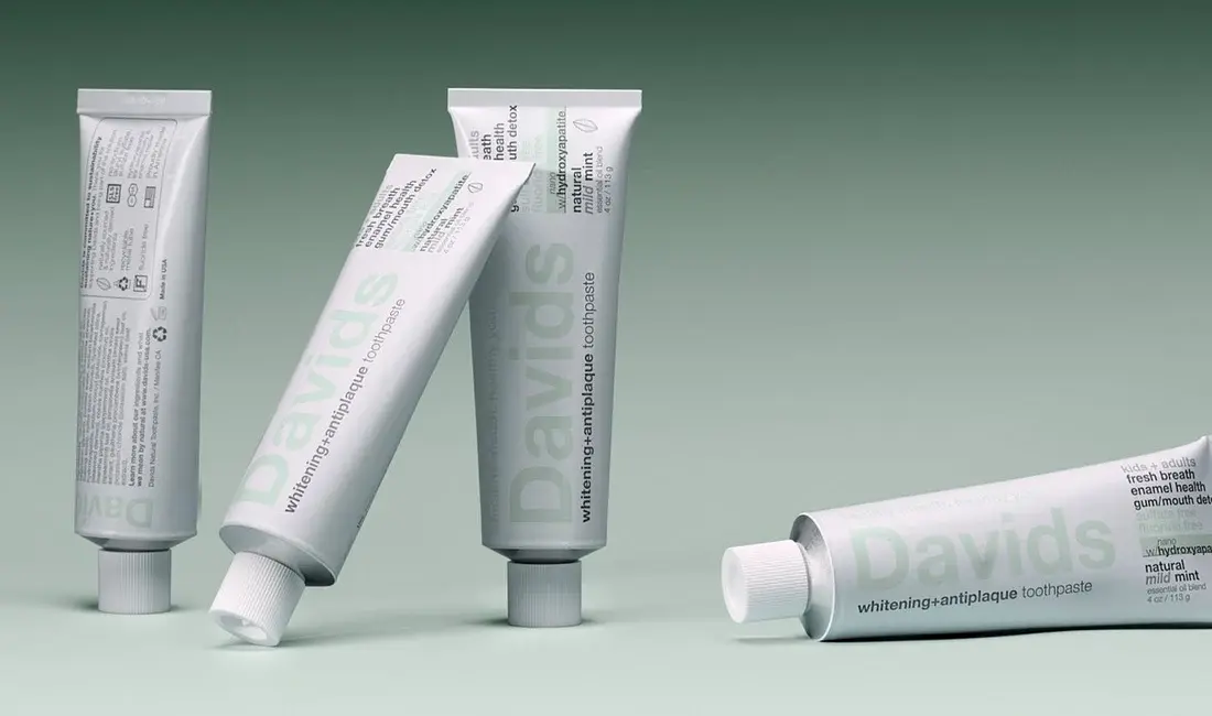 Davids toothpaste tubes standing and lying at angles against a soft green backdrop