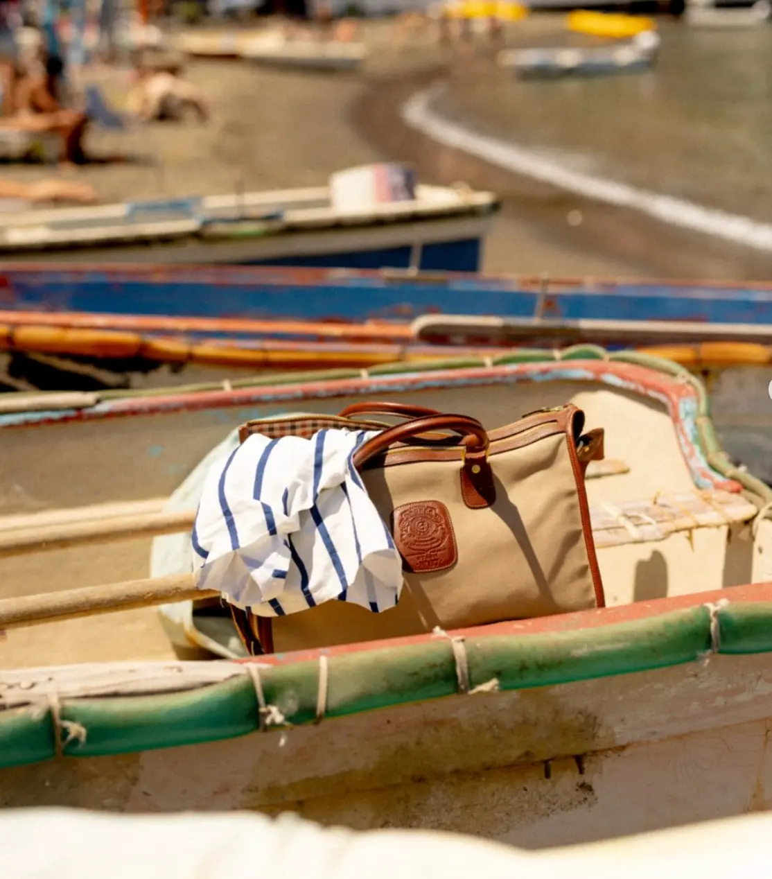 A Ghurka canvas and leather bag with a striped shirt draped over it, resting in a rowing boat on a beach