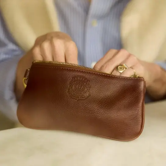 Hands opening a brown Ghurka leather zip pouch