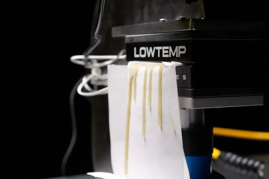 A Lowtemp heat press with pale strands pressed out onto a sheet of white paper