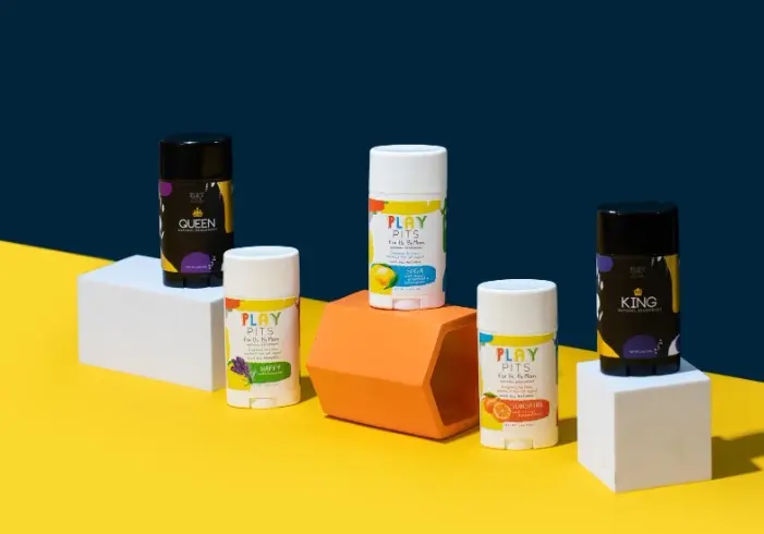 Five Play Pits deodorant sticks on white and orange blocks against a yellow and navy backdrop