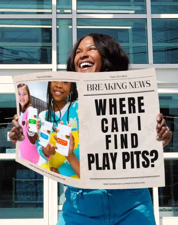 A woman laughing behind a newspaper headlined “Where can I find Play Pits?”