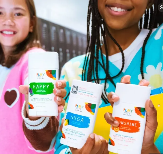 Two smiling girls holding Play Pits deodorant sticks in the Happy, Suga and Sunshine scents