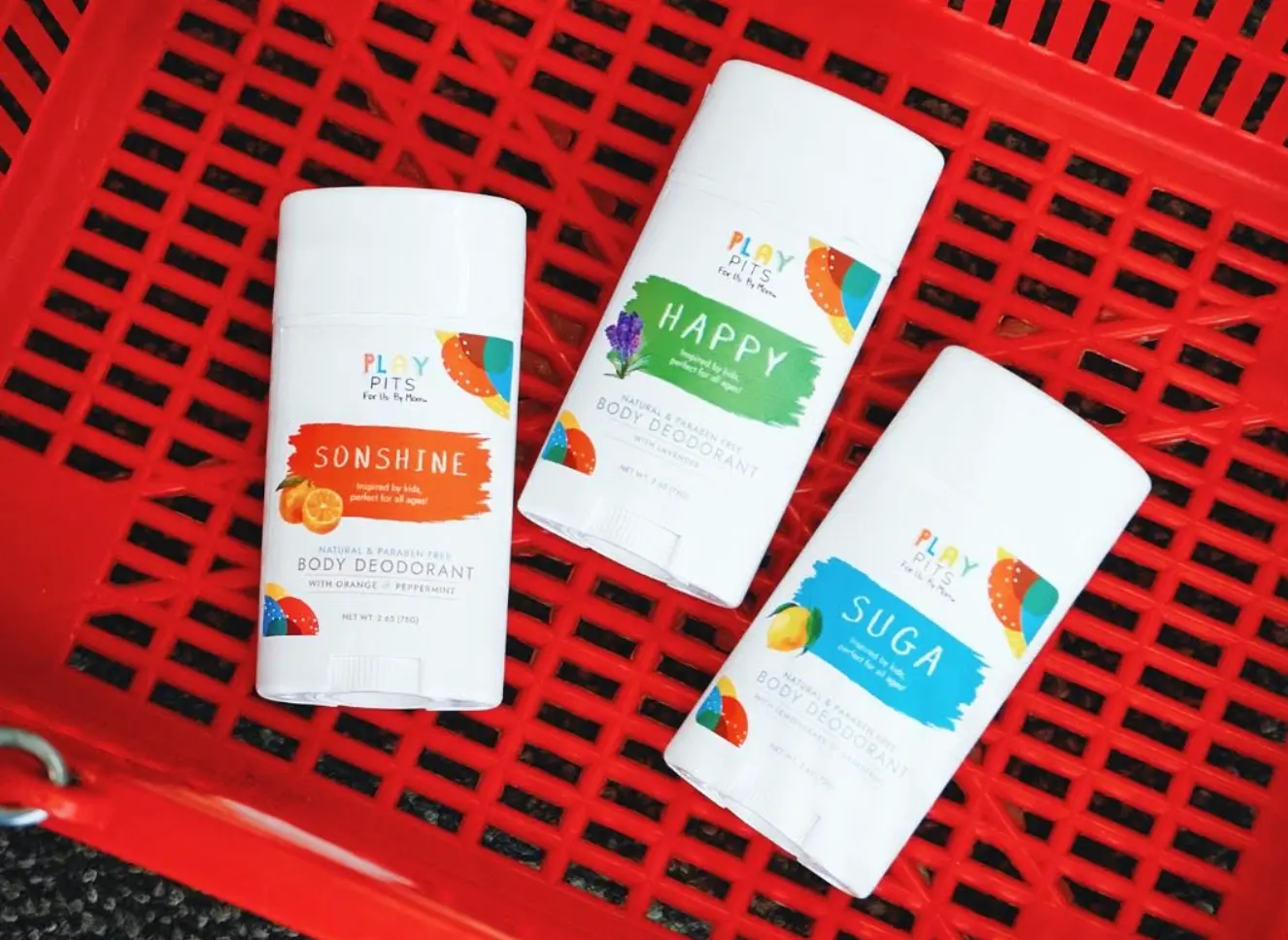 Play Pits Sonshine, Happy and Suga deodorants lying in a red shopping basket, seen from above