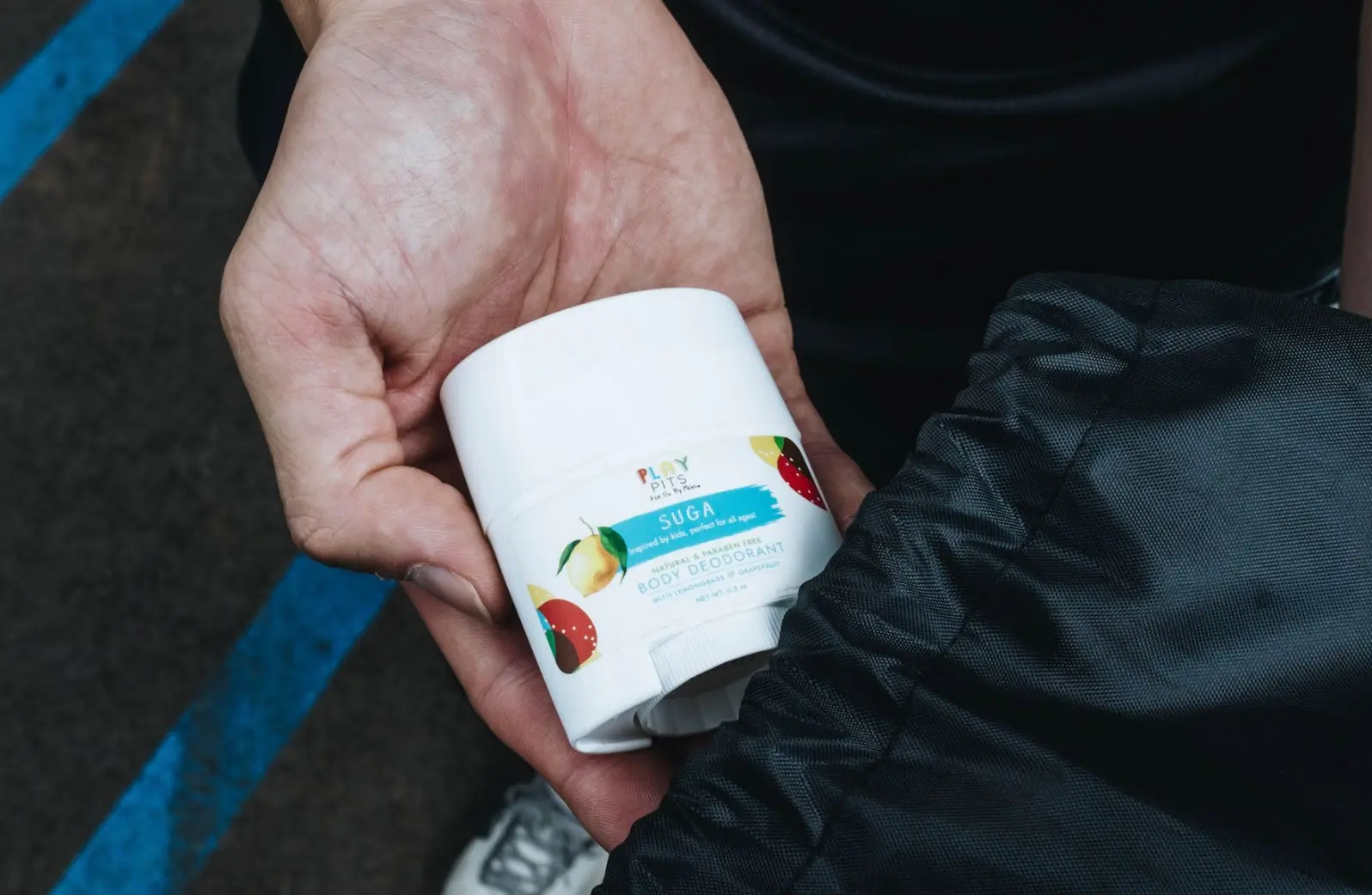 A hand holding a Play Pits Suga deodorant stick, seen from above