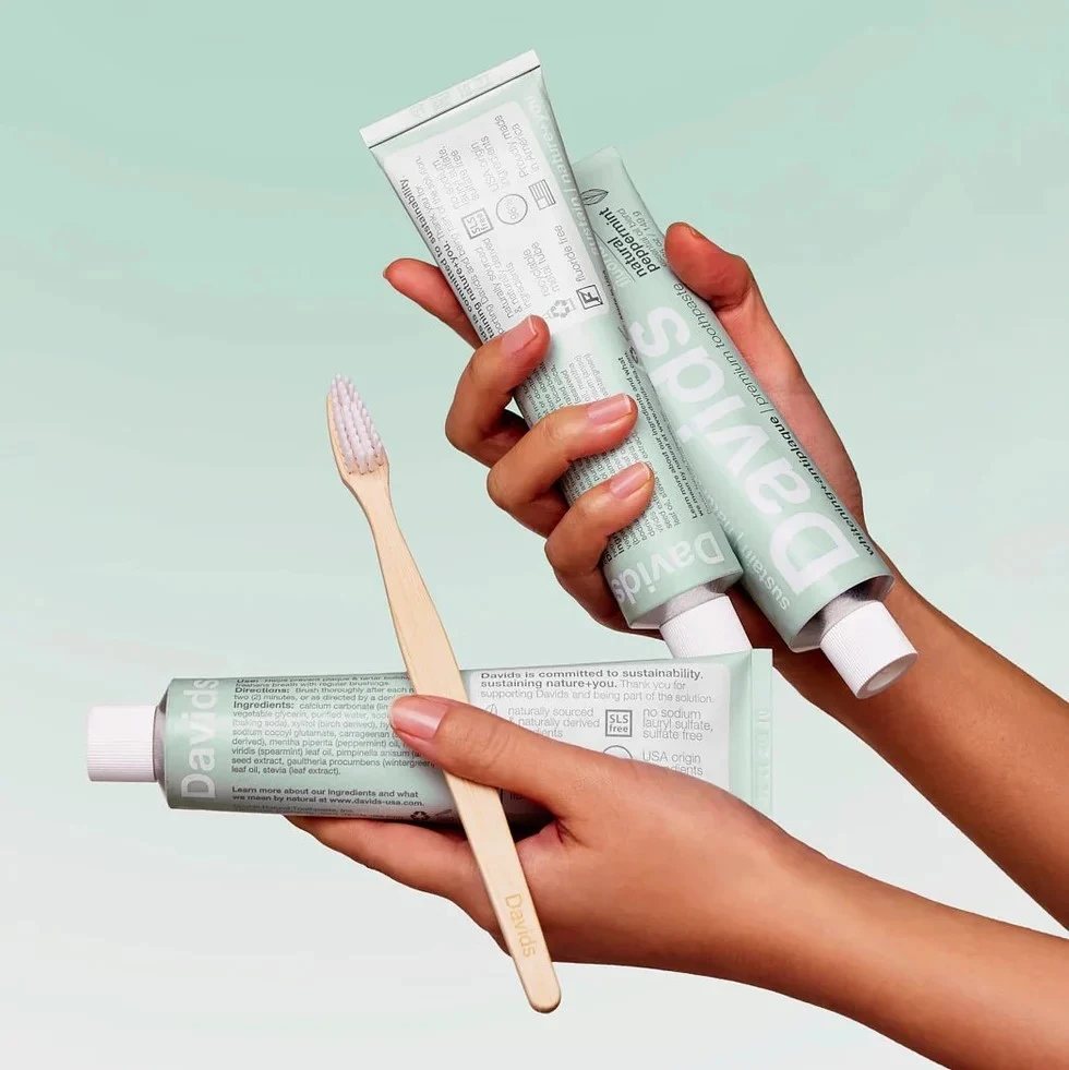 Hands holding three tubes of Davids natural toothpaste and a bamboo toothbrush