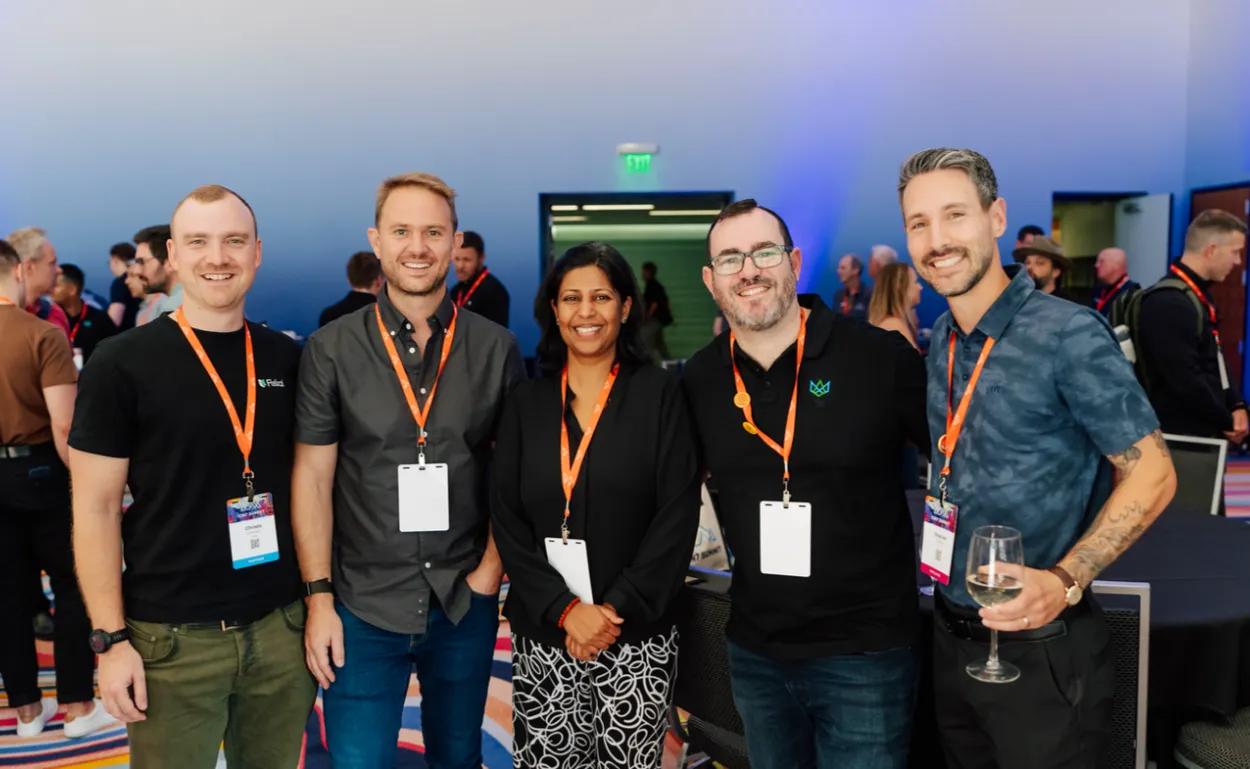 Four men and a woman smiling together in a conference hall, wearing orange Cin7 Summit lanyards